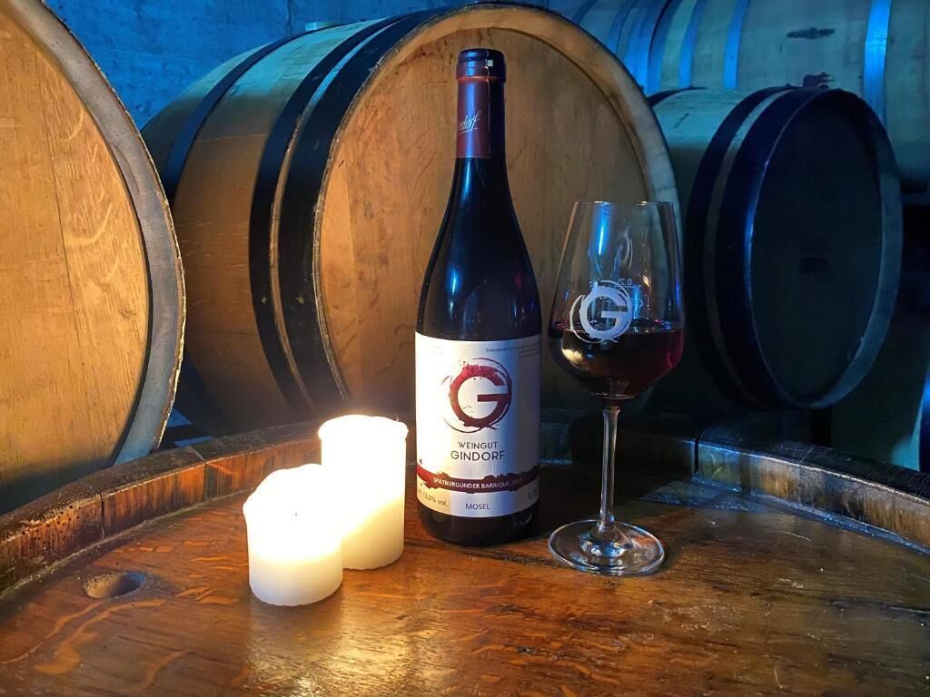 Une bouteille de vin avec une étiquette, un verre de vin rouge et deux bougies posées sur un tonneau en bois.