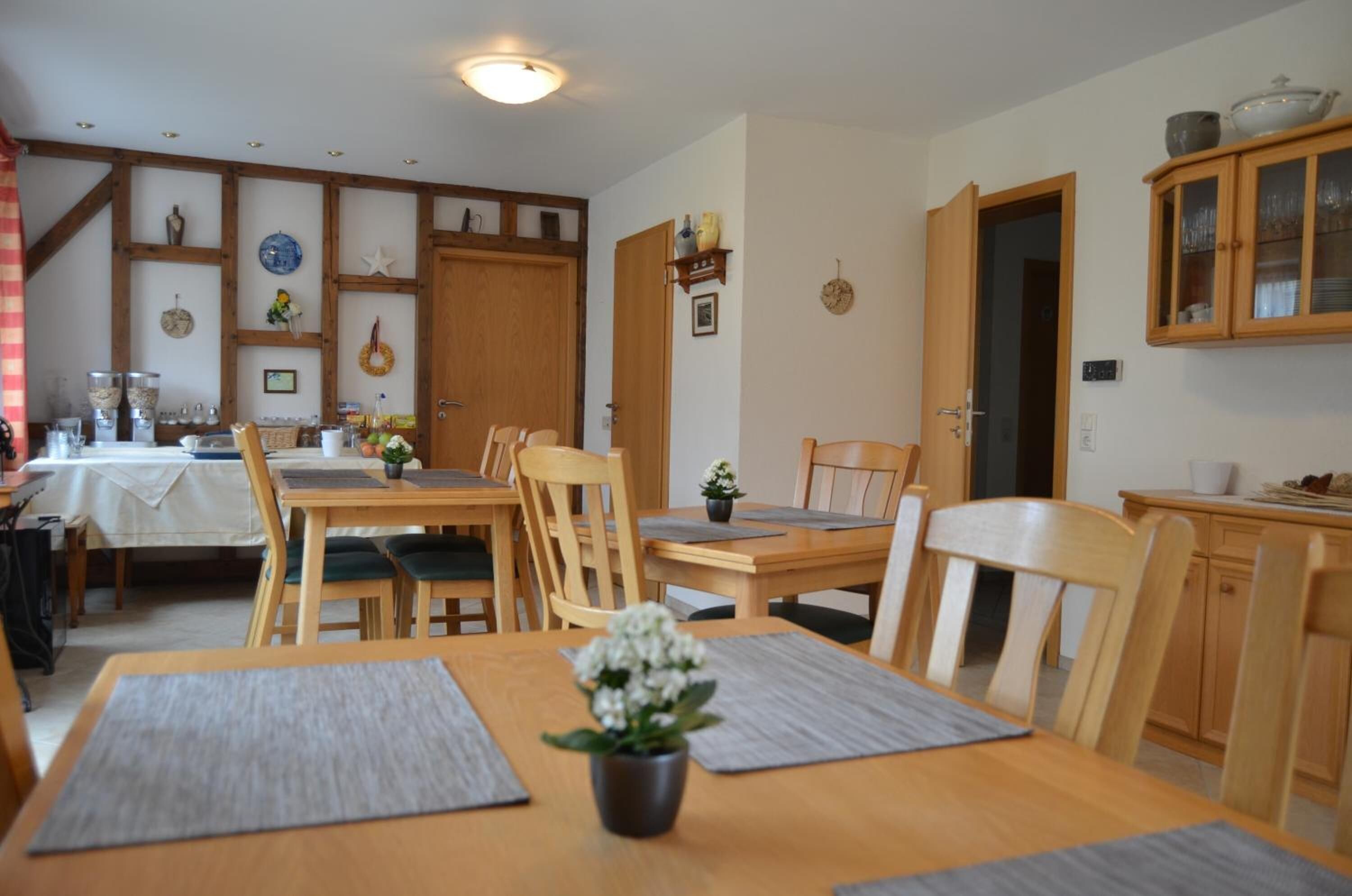 A dining area with wooden tables and chairs, a small potted plant, and a wooden cabinet with glass doors.