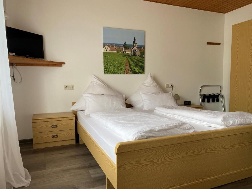 Un dormitorio con una cama de madera, una mesita de noche, un televisor en un estante y un cuadro de un viñedo en la pared.