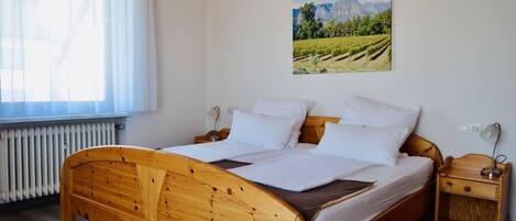 A wooden bed with white bedding, a bedside table with a lamp, and a window with sheer curtains.