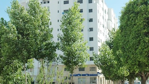 Un immeuble à plusieurs étages, doté d’un toit plat, entouré d’un espace verdoyant bien entretenu, agrémenté de jeunes arbres.
