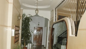 Un couloir doté d’un sol en marbre, de plantes en pot, d’un grand miroir et d’un escalier.