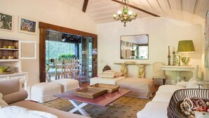 A cozy living room with white furniture, a chandelier, and a view of the garden through glass doors. - Village dos Ossos (Búzios)
