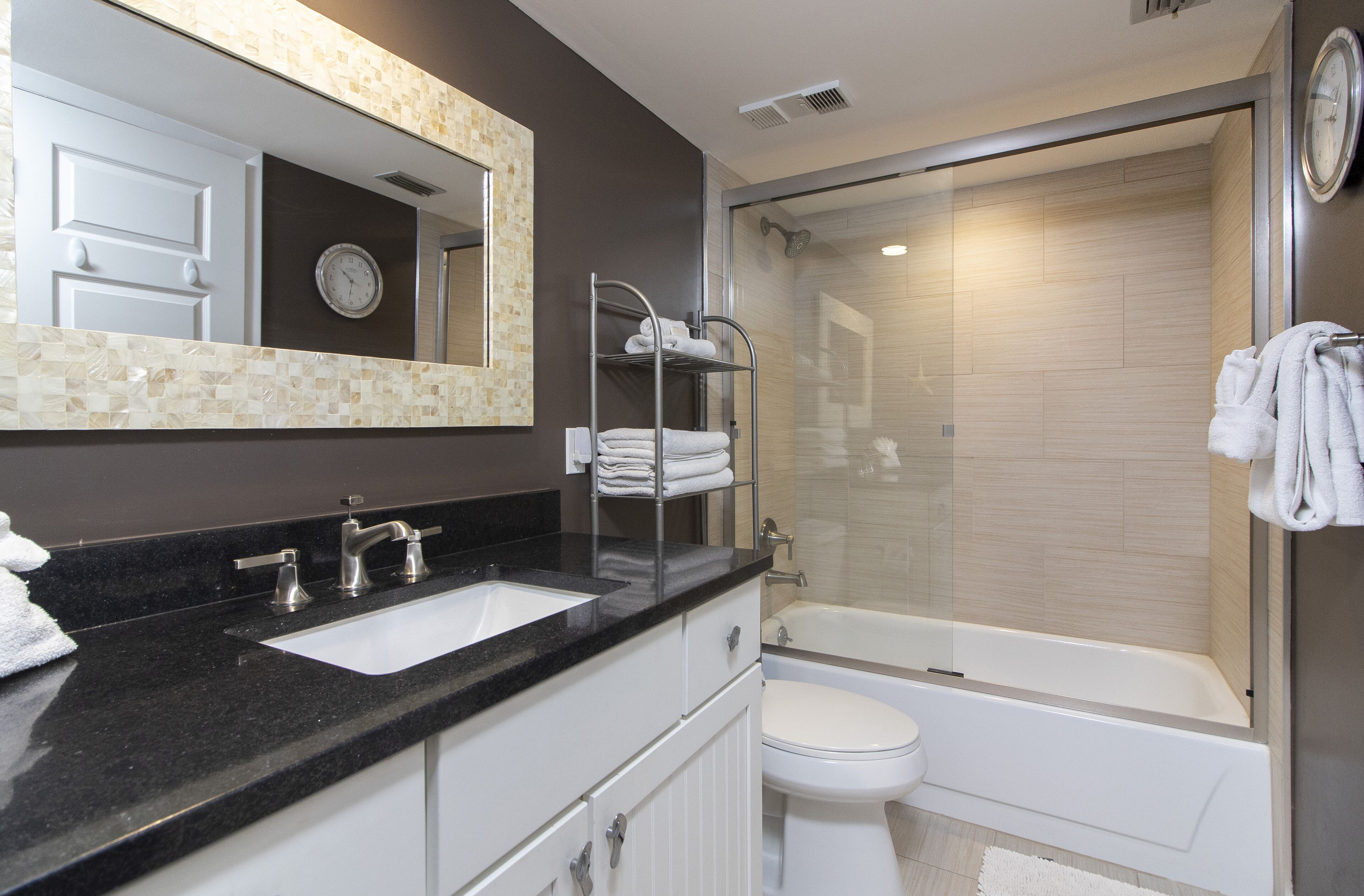 Un baño moderno con encimera negra, lavabo blanco y ducha con mampara de vidrio.