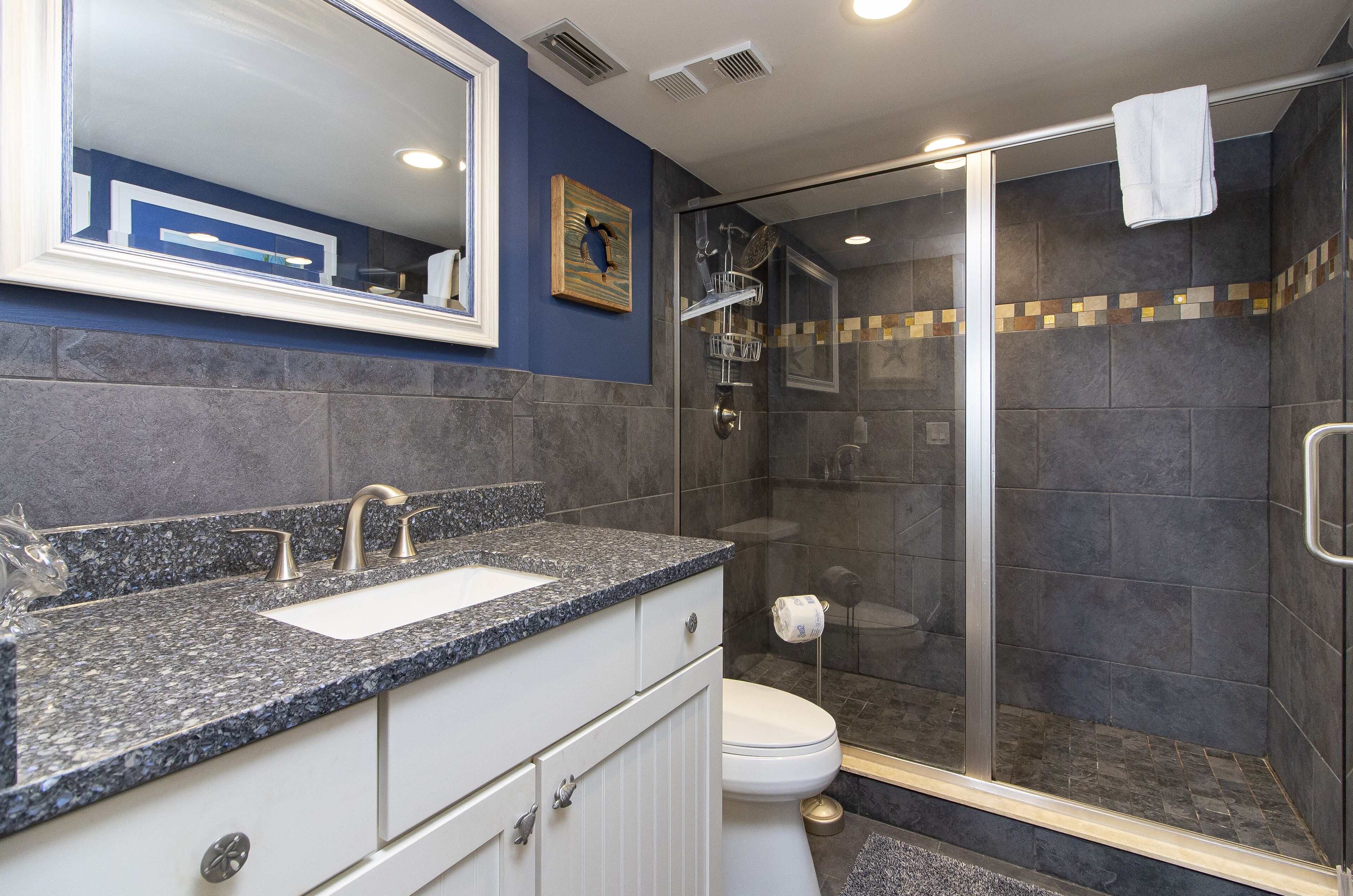 A modern bathroom with a granite countertop, a white sink, and a glass-enclosed shower.