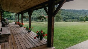 A wooden deck with potted flowers and a bench, overlooking a grassy field and forested hills. - Potter County Gasthaus - Full Lodge for Rent (Shinglehouse)