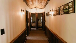 A narrow hallway with wooden paneling and a carpeted floor, leading to a room with a bed and a window. - Potter County Gasthaus - Full Lodge for Rent (Shinglehouse)