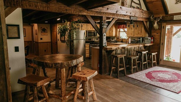 A rustic kitchen with wooden beams, a large wooden table, and bar stools. - Potter County Gasthaus - Full Lodge for Rent (Shinglehouse)