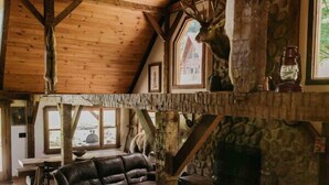 A rustic interior with a stone fireplace, wooden beams, and a leather sofa. - Potter County Gasthaus - Full Lodge for Rent (Shinglehouse)