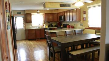 A kitchen with wooden cabinets, a dining table with chairs, a refrigerator, and a ceiling fan.