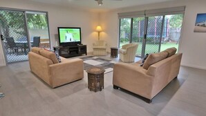 Ein geräumiges Wohnzimmer mit beigen Sofas, einem Fernseher und einem Deckenventilator.
