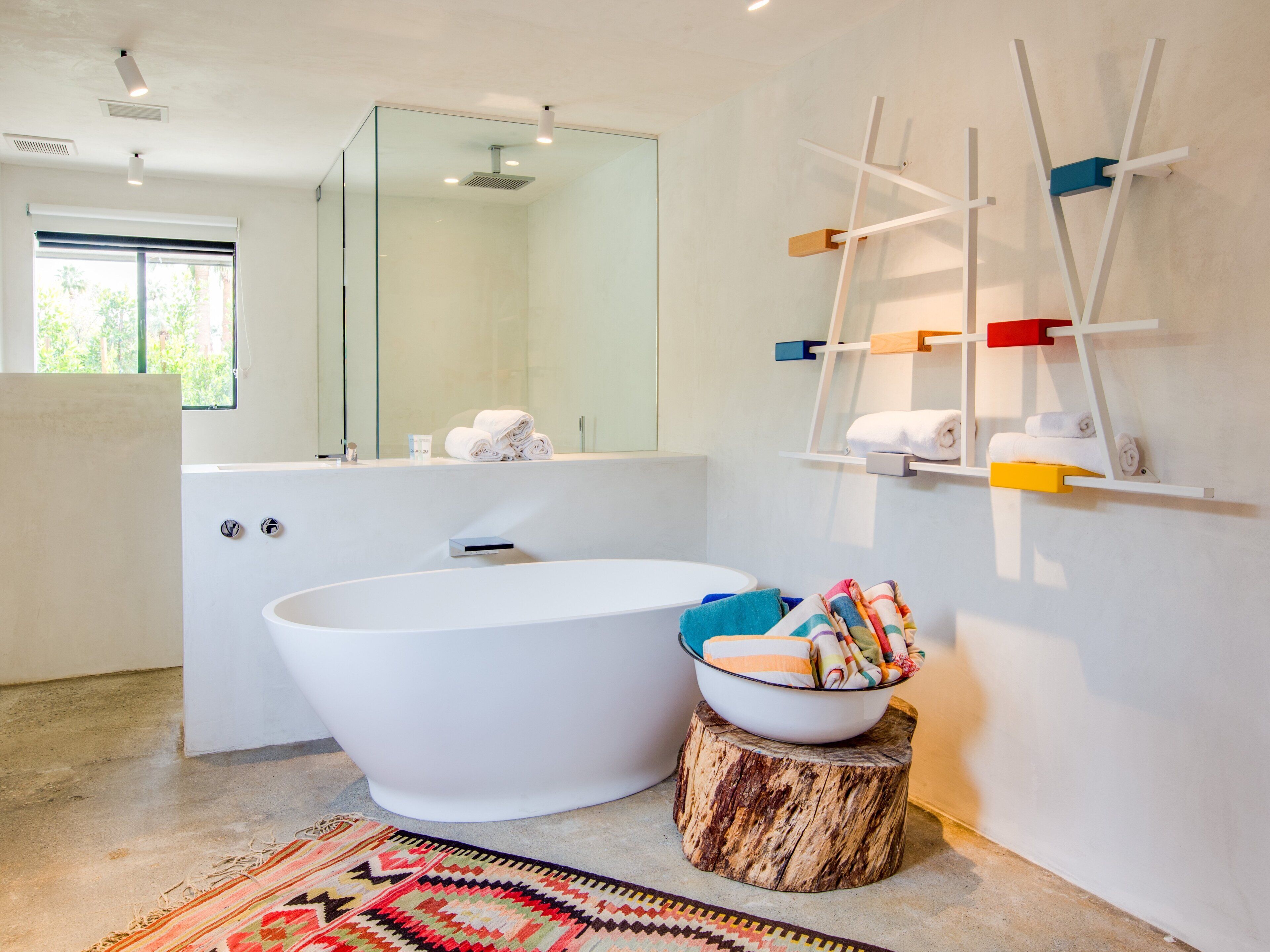 Un baño moderno con una bañera independiente, un taburete de madera con un cuenco de toallas y un perchero de toallas en la pared.