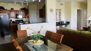 A modern kitchen with dark wooden cabinets, a black refrigerator, and a microwave. There is a dining area with wicker furniture and a glass table. - WATER VIEW*4 Bedroom/Elevator/5 Star Condo* DISNEY Area (Kissimmee)