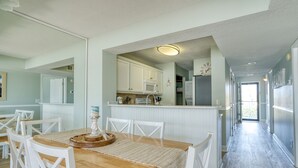 Een moderne keuken met witte kasten, een magnetron en een koelkast. Er is een eethoek met een houten tafel en witte stoelen.