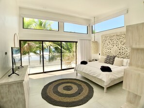 A modern bedroom with a large bed, a view of palm trees, and a balcony.