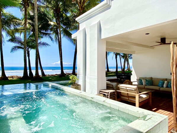 A pool area with a view of the ocean, surrounded by palm trees and a white building.