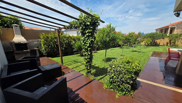 Un patio con una parrilla, una pérgola cubierta de plantas trepadoras y un césped cuidado.