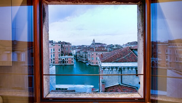 Udsigt gennem et vindue af en kanal i Venedig, Italien, hvor bygninger og både ses.