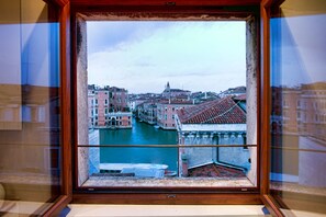 A view through a window of a canal in Venice, Italy, with buildings and boats visible.