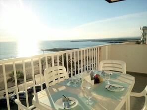 Un balcon avec une table dressée pour deux personnes, donnant sur une plage et la mer.