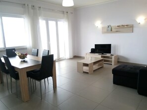 Una sala de estar moderna con comedor, un televisor de pantalla plana y una mesa de centro de madera clara.