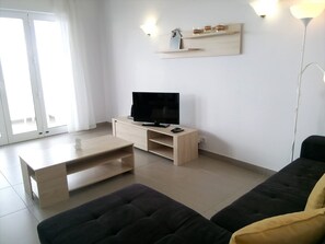 Una sala de estar moderna con un televisor de pantalla plana, una mesa de centro de madera, un sofá negro y un cojín amarillo.