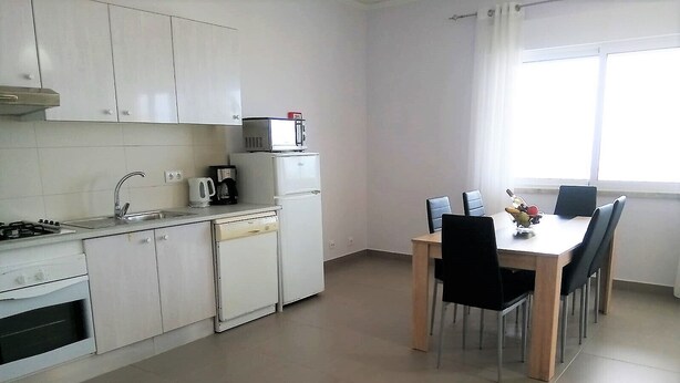 Une cuisine de taille réduite avec des meubles blancs, une cuisinière, un four à micro-ondes et un réfrigérateur. On y trouve une table à manger avec quatre chaises.