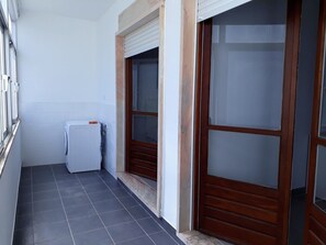 Um corredor estreito com piso de azulejos, um radiador branco e uma porta de madeira com painel de vidro jateado.