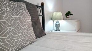 Un lit bien fait, agrémenté d’oreillers à motifs, une table de chevet avec une lampe et une petite plante.