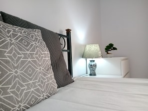 Un lit bien fait, agrémenté d’oreillers à motifs, une table de chevet avec une lampe et une petite plante.