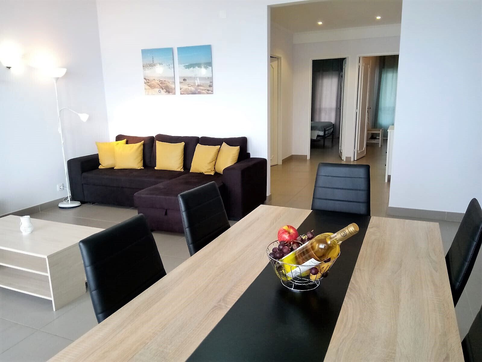 A modern living room with a dark-colored sofa, a dining table with chairs, and a bottle of champagne on the table.
