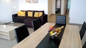 Un salon moderne avec un canapé de couleur foncée, une table à manger avec des chaises et une bouteille de champagne posée sur la table.