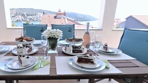 A table set for a meal with plates of cake and glasses of water, overlooking a town with red-roofed buildings.