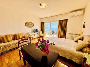 A hotel room with a bed, a sofa, a TV, a table with flowers, and a balcony with a view.