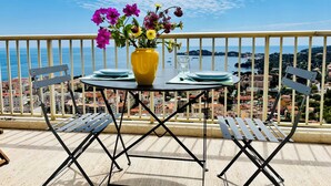 A balcony with a table set for two, a yellow vase with flowers, and a view of the sea and town. - Luxury Apartment block (Villefranche-Sur-Mer)