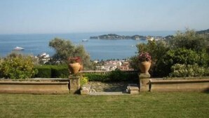 A view of a coastal landscape with a grassy area, two large planters, and a distant view of the sea and a small island. - Luxury Apartment block (Villefranche-Sur-Mer)
