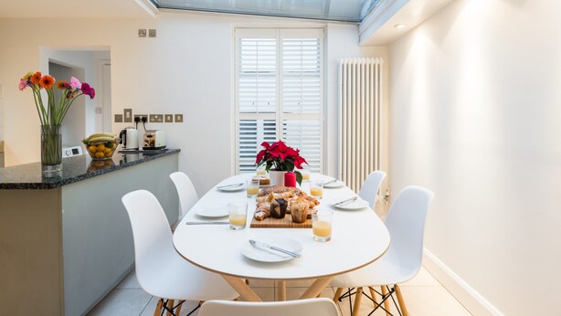 Zona pranzo moderna con soffitto in vetro, pareti bianche e tavolo centrale apparecchiato per quattro persone.