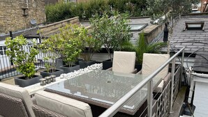 Una terrazza sul tetto con tavolo in vetro, mobili in vimini e piante in vaso.