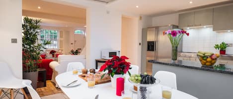 Una cocina moderna con comedor, que incluye una mesa blanca dispuesta con platos, cubiertos y un jarrón de flores.