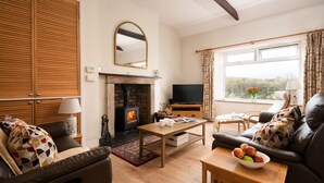 A cozy living room with a fireplace, wooden furniture, a television, and a view of the outdoors. - Cosy pet friendly farm cottage, 15 minutes to Northumberland coast! (Berwick-upon-Tweed)