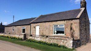 A stone house with a sloped roof, a white door, and a window with a white frame. - Cosy pet friendly farm cottage, 15 minutes to Northumberland coast! (Berwick-upon-Tweed)