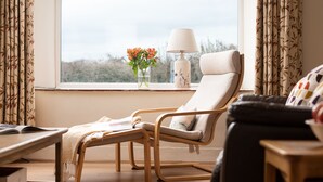 A room with a wooden chair, a small table with a lamp, and a window with curtains. - Cosy pet friendly farm cottage, 15 minutes to Northumberland coast! (Berwick-upon-Tweed)