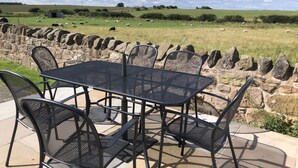 A patio with a table and chairs overlooking a grassy field with sheep. - Cosy pet friendly farm cottage, 15 minutes to Northumberland coast! (Berwick-upon-Tweed)