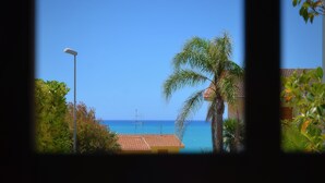 A view through a window of a tiled patio area with a palm tree and a building with a tiled roof. - Guest House Adele-Marina Di Ragusa (Marina di Ragusa)