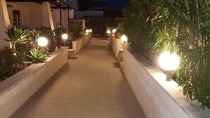 A paved pathway flanked by planters with illuminated globes, leading to a building with a modern design and a thatched roof structure. - Guest House Adele-Marina Di Ragusa (Marina di Ragusa)
