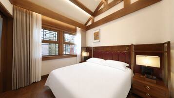 A hotel room with a large bed, wooden headboard, bedside lamps, a window with curtains, and a framed picture on the wall.