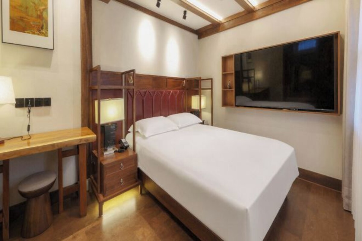 A hotel room with a bed, bedside table, lamp, and a large window.