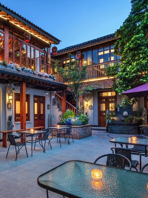Un patio con mobiliario exterior, una escalera y un edificio con balcones de madera.