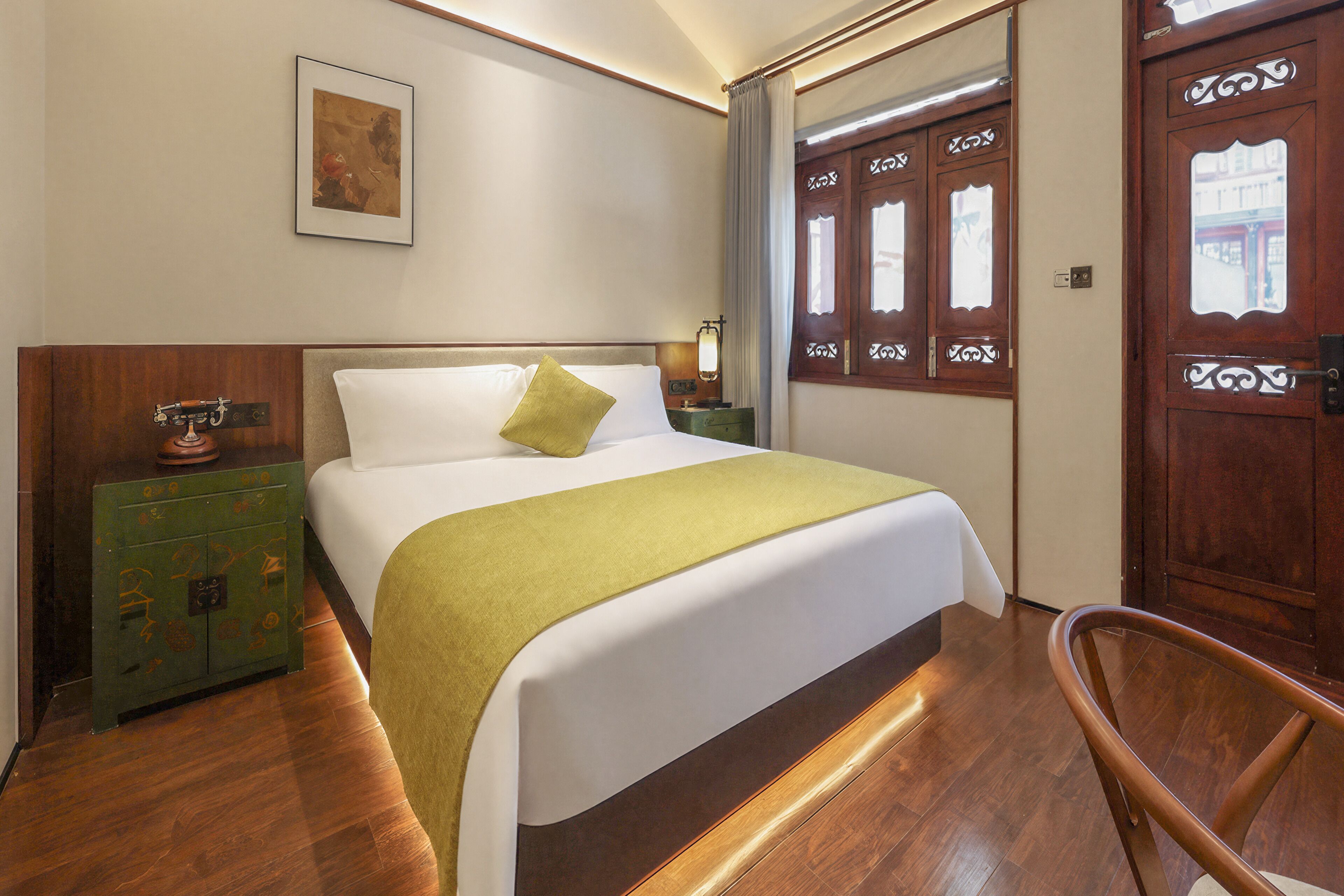 A hotel room with a bed, a green chest of drawers, a wooden door, and a framed picture on the wall.