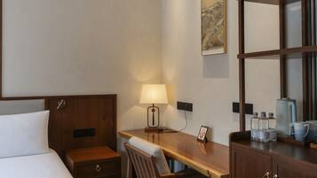 A hotel room with a bed, a desk, a chair, a lamp, a picture frame, a cabinet, and a coffee maker.